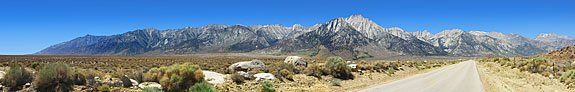 On the road west to Whitney Portal, the wall of the eastern Sierra rises up from the flat Owens Valley. Mt. Whitney appears much lower than the closer front range peaks. Whitney is pyramid-shaped with two chimney peaks to the left, directly above the first yellow dash in the road.