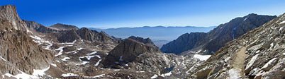 Panorama east with Mt. Whitney (L) above the snow-streaked terrain of the Mountaineer's Route to Trail Camp (lake, center right). The rock in the center is Wutan's Throne. The trail from Whitney Portal came through the slot valley at center right.